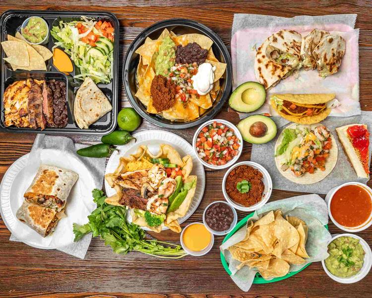 A spread of dishes on a wood table — grilled meat, rice, beans, tortillas and a drink